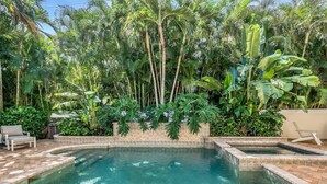 A pool surrounded by lush tropical plants and a tiled deck with a lounge chair. - Casa Captiva - Ground Level 5 BR Luxe Villa with Grotto Pool, Steps to Beach (Captiva)