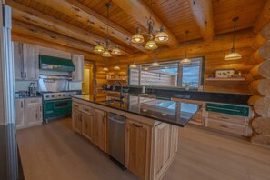 A log cabin kitchen with wooden cabinets, a central island, stainless steel appliances, and pendant lighting. - FOXFHILL: 6,000+ sq ft log estate, 4BR/5BA sleeps 16. (Otis Orchards)