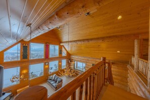 A log cabin interior with a loft bedroom, large windows, wooden beams, and a chandelier. - FOXFHILL: 6,000+ sq ft log estate, 4BR/5BA sleeps 16. (Otis Orchards)