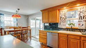 A kitchen with wooden cabinets, a dishwasher, and a dining area with a table and chairs. - 12 Mi to Dtwn Denver: Home w/ Fenced Backyard! (Northglenn)