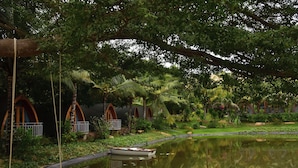 A serene garden with a pond, wooden swing chairs, and treehouses.
