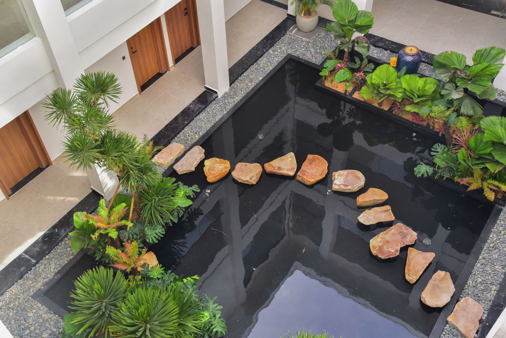 Ein moderner Innenhofgarten mit einem zentralen Wasserspiel, umgeben von verschiedenen Pflanzen und Steinen.