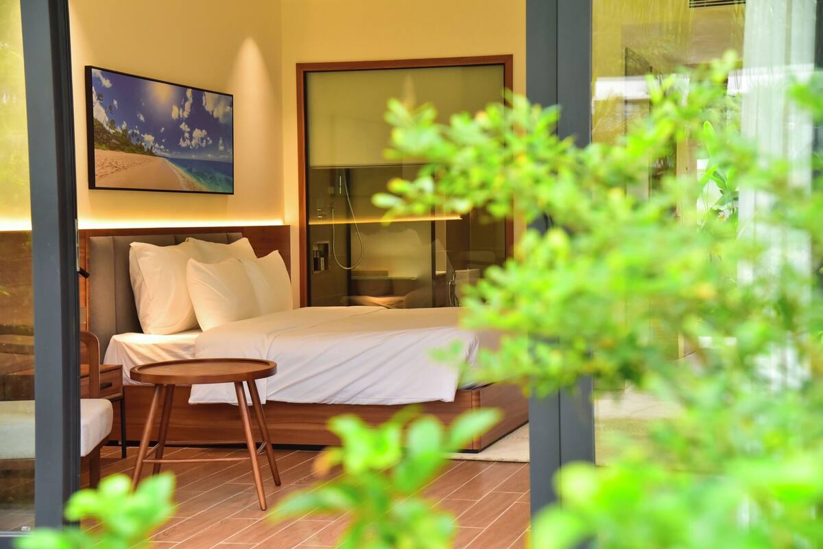 Una habitación de hotel moderna con cama, una pequeña mesa redonda, zona de ducha y un cuadro en la pared.