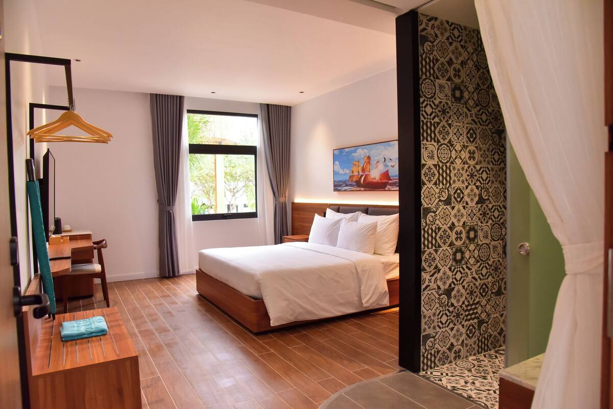 Habitación de hotel con cama, escritorio, silla, lámpara colgante y ventana con cortinas.