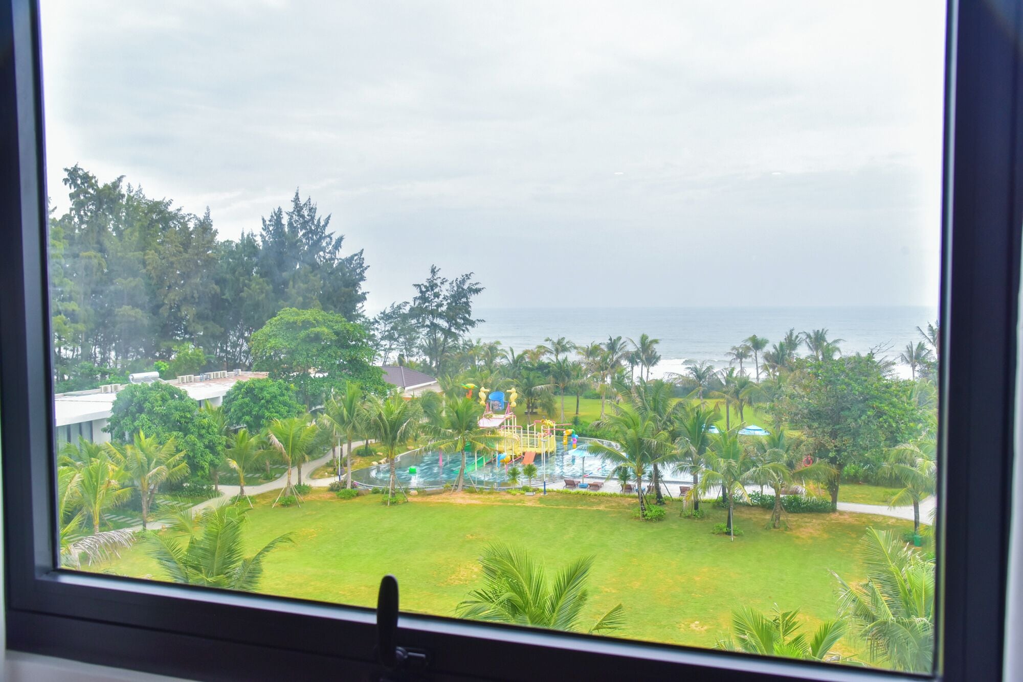 Vista de un complejo turístico con zona de piscina, palmeras y vista al océano.