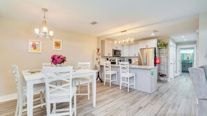 Una cocina moderna con armarios blancos, una isla central y un comedor con sillas y una mesa blancos.