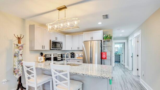 Una cocina moderna con armarios blancos, encimeras de granito, electrodomésticos de acero inoxidable y una lámpara decorativa.
