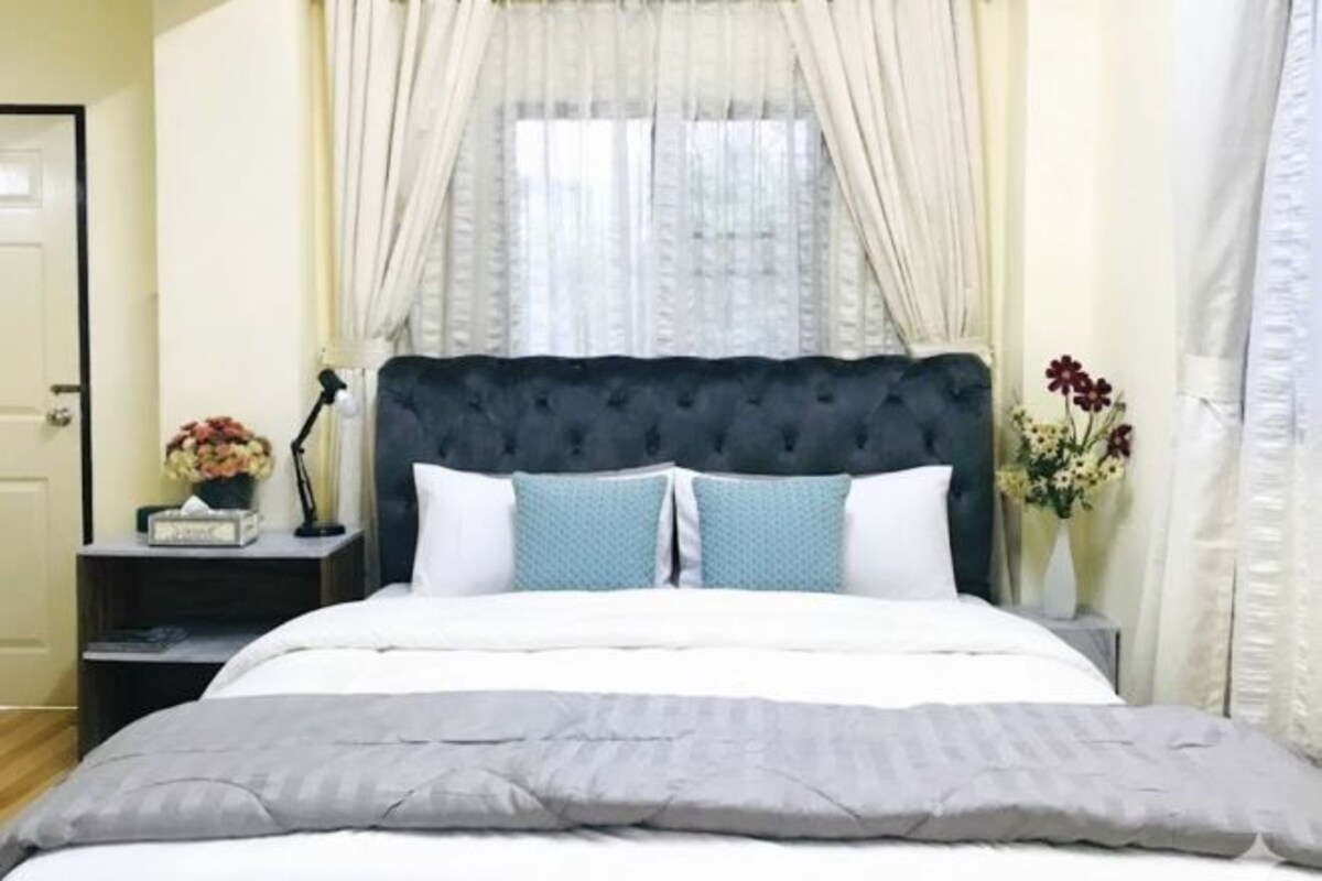 A neatly arranged bedroom with a tufted headboard, a white bedspread, and a grey blanket.
