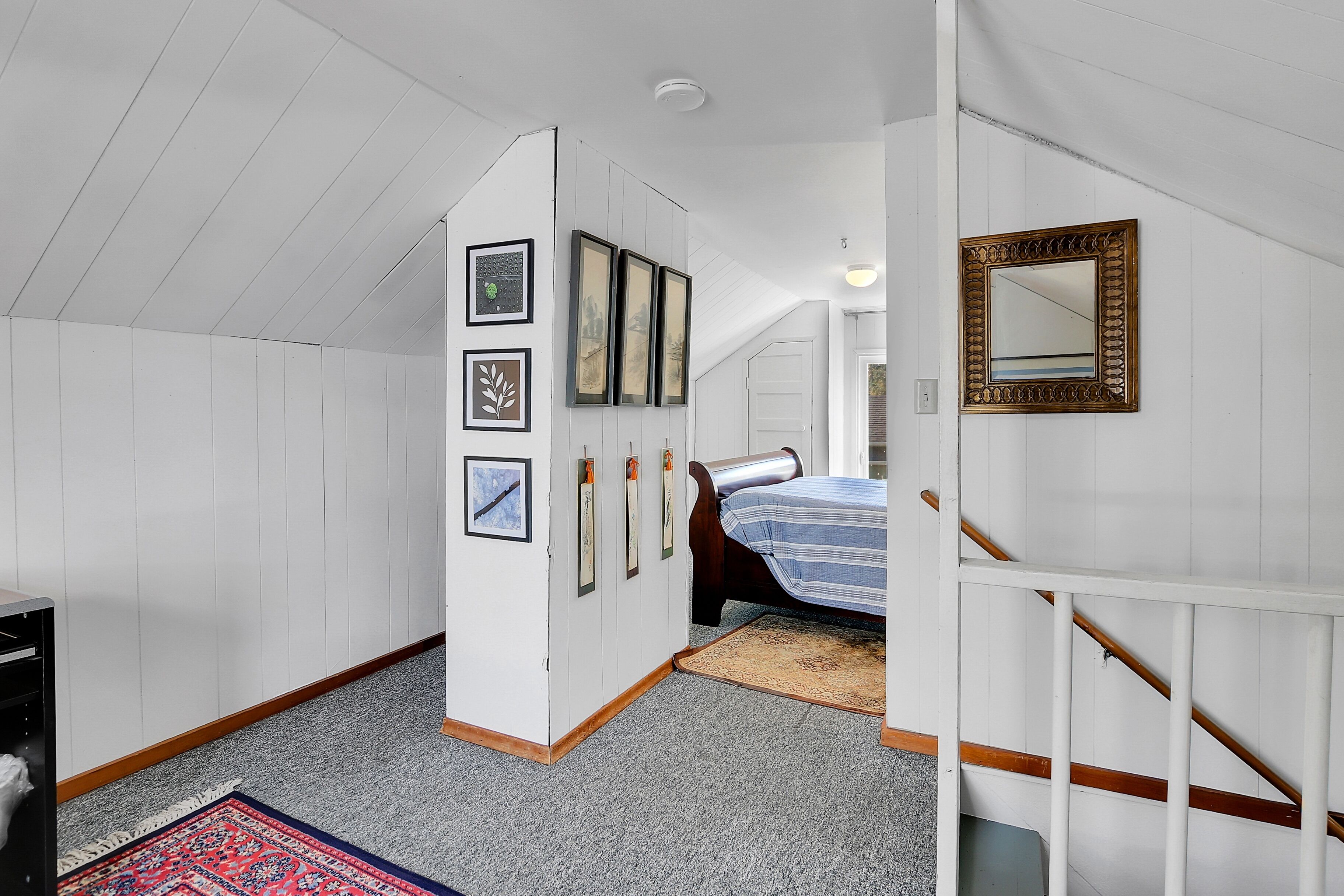 A bedroom with a bed, a wardrobe, a mirror, and framed pictures on the wall.