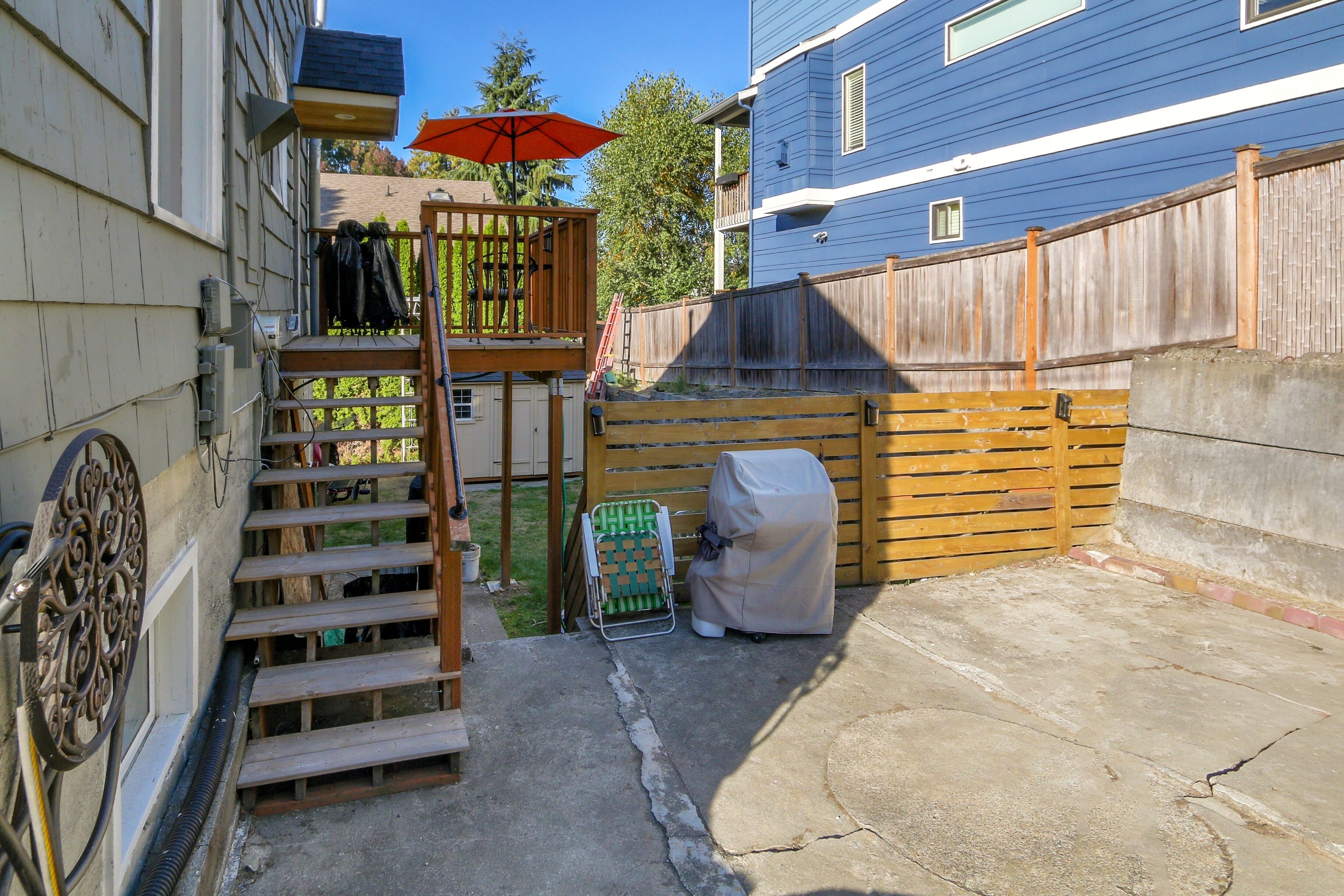 Un patio trasero con una terraza de madera, una parrilla cubierta y un patio de concreto.