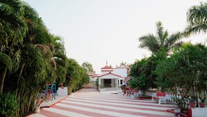 A pathway leading to a building with a red roof, surrounded by palm trees and potted plants. - khodal Resort (Girgadhada)