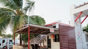 A small building with a red and white exterior, a staircase leading to a covered entrance, and a palm tree nearby. - khodal Resort (Girgadhada)