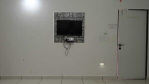 A room with a television mounted on the wall, a door, and a tiled floor. - khodal Resort (Girgadhada)
