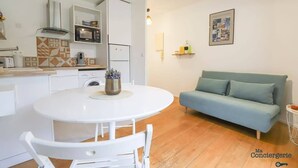 A compact living space with a kitchenette, a dining table, a sofa, and a framed collage on the wall. - Lardenne - Parking, hippodrome Zenith (Toulouse)