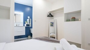 A modern hotel room with a bed, a bathroom with a blue accent wall, and a small shelf with toiletries. - Lardenne - Parking, hippodrome Zenith (Toulouse)