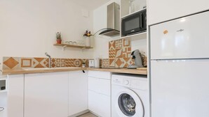A compact kitchen with white cabinets, a washing machine, a microwave, and a refrigerator. - Lardenne - Parking, hippodrome Zenith (Toulouse)