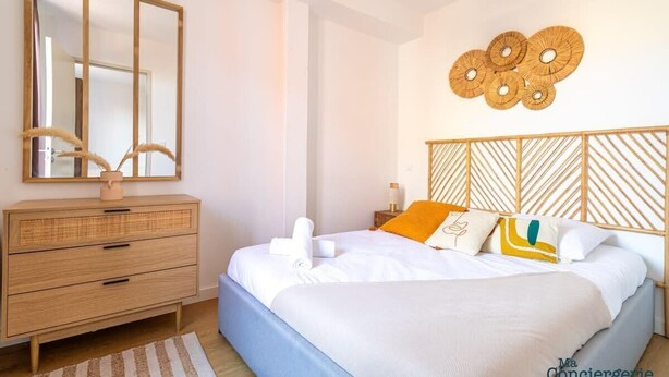 Ein Schlafzimmer mit einem Bett, einer Holzkommode, einem Spiegel und einer Wanddekoration.