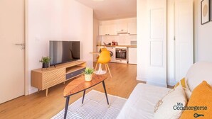 Ein modernes Wohnzimmer mit Fernseher, Holzschrank und Essbereich mit gelbem Stuhl.