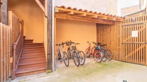 Ein überdachter Außenbereich mit einer Holztreppe, die zu einem Gebäude führt, und mehreren Fahrrädern, die an einer Wand lehnen.
