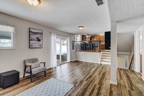 A spacious living area with hardwood flooring, a gray sofa, a patterned rug, and a large window with a view.