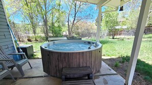 Een houten jacuzzi onder een overdekt terras, met een bankje en een klein tafeltje.