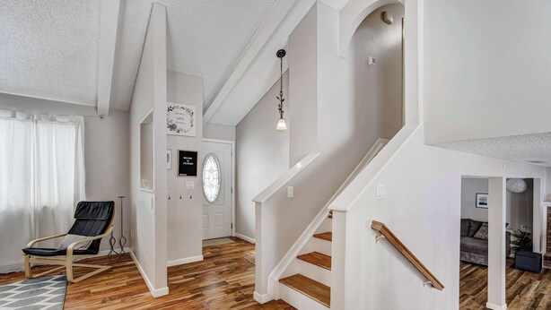 Een ruime woonkamer met houten vloer, een zwarte leren fauteuil, een trap met houten treden en een witte deur met een rond raam.