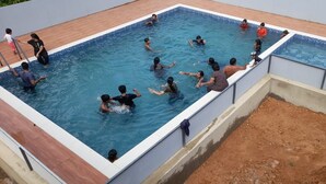 A swimming pool with multiple people in the water, surrounded by a tiled deck and a concrete border. - HIMANI HERITAGE (Madikeri)