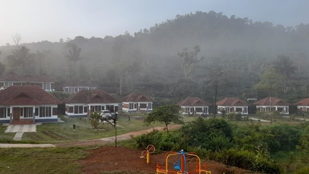 A residential area with multiple houses, a playground, and a hilly backdrop. - HIMANI HERITAGE (Madikeri)