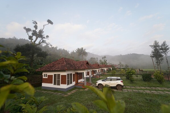 A row of white buildings with red roofs, surrounded by greenery and a misty landscape. - HIMANI HERITAGE (Madikeri)