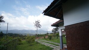 A house with a stone pathway leading to a door, surrounded by lush greenery and mountains in the background. - HIMANI HERITAGE (Madikeri)
