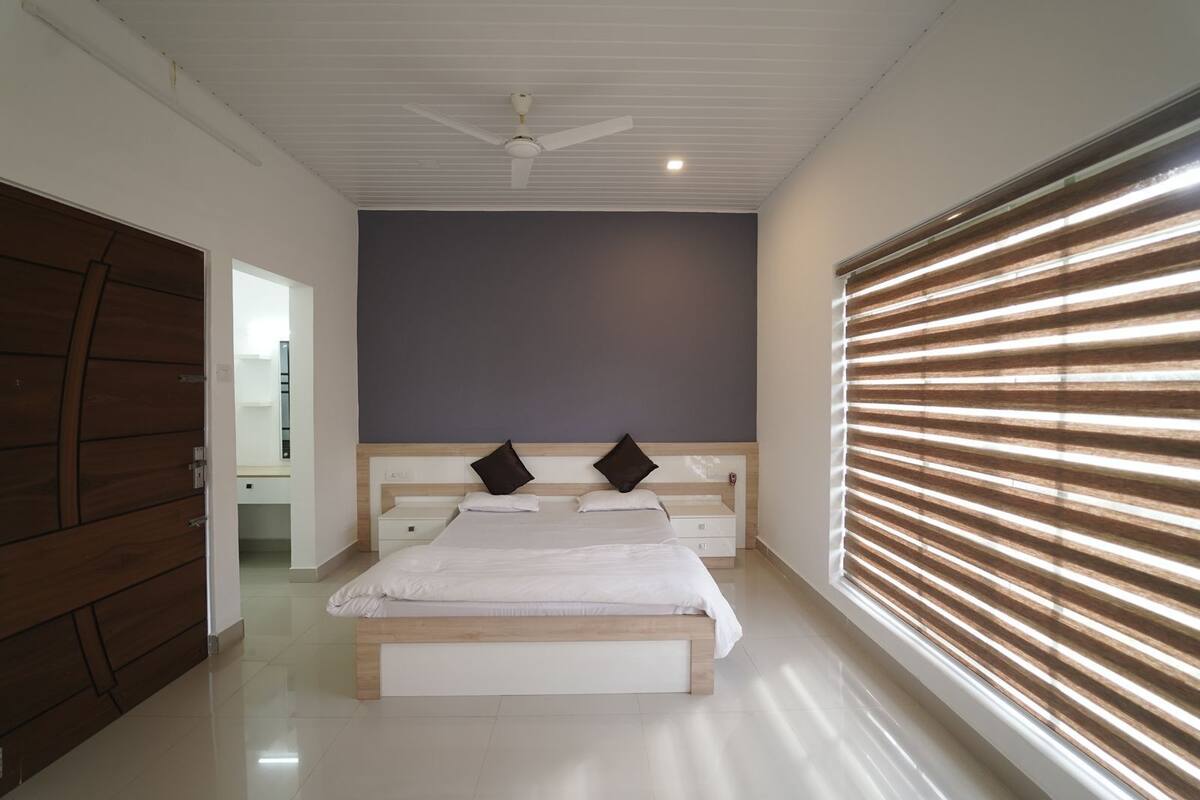 A bedroom with a large bed, two bedside tables, a ceiling fan, and a window with blinds.