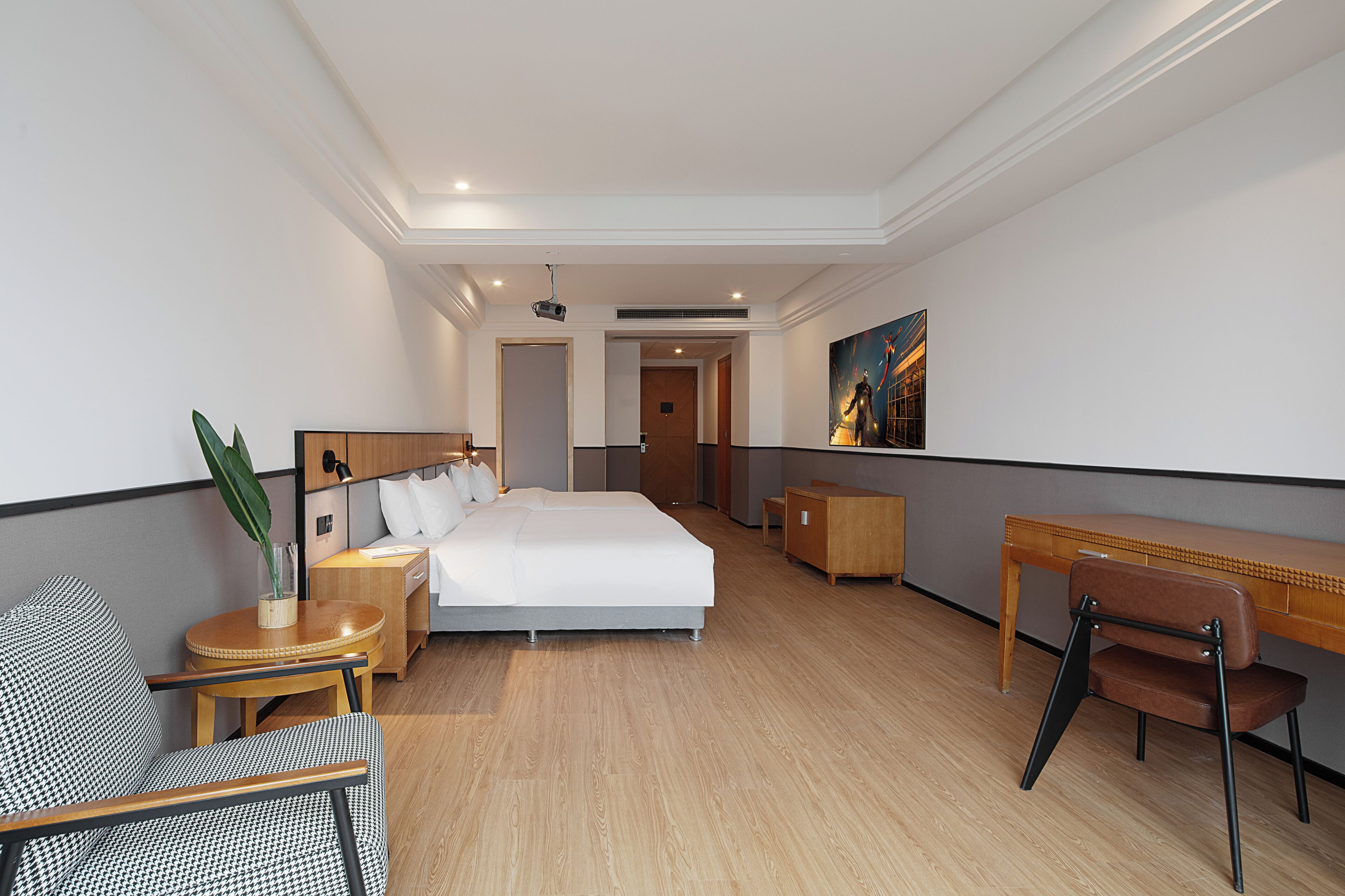 Een hotelkamer met een groot bed, een bureau, een stoel, een kleine tafel met een plant en een schilderij aan de muur.