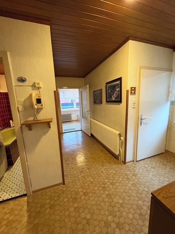 A hallway with a tiled floor, a radiator, a door, and a wall-mounted telephone.