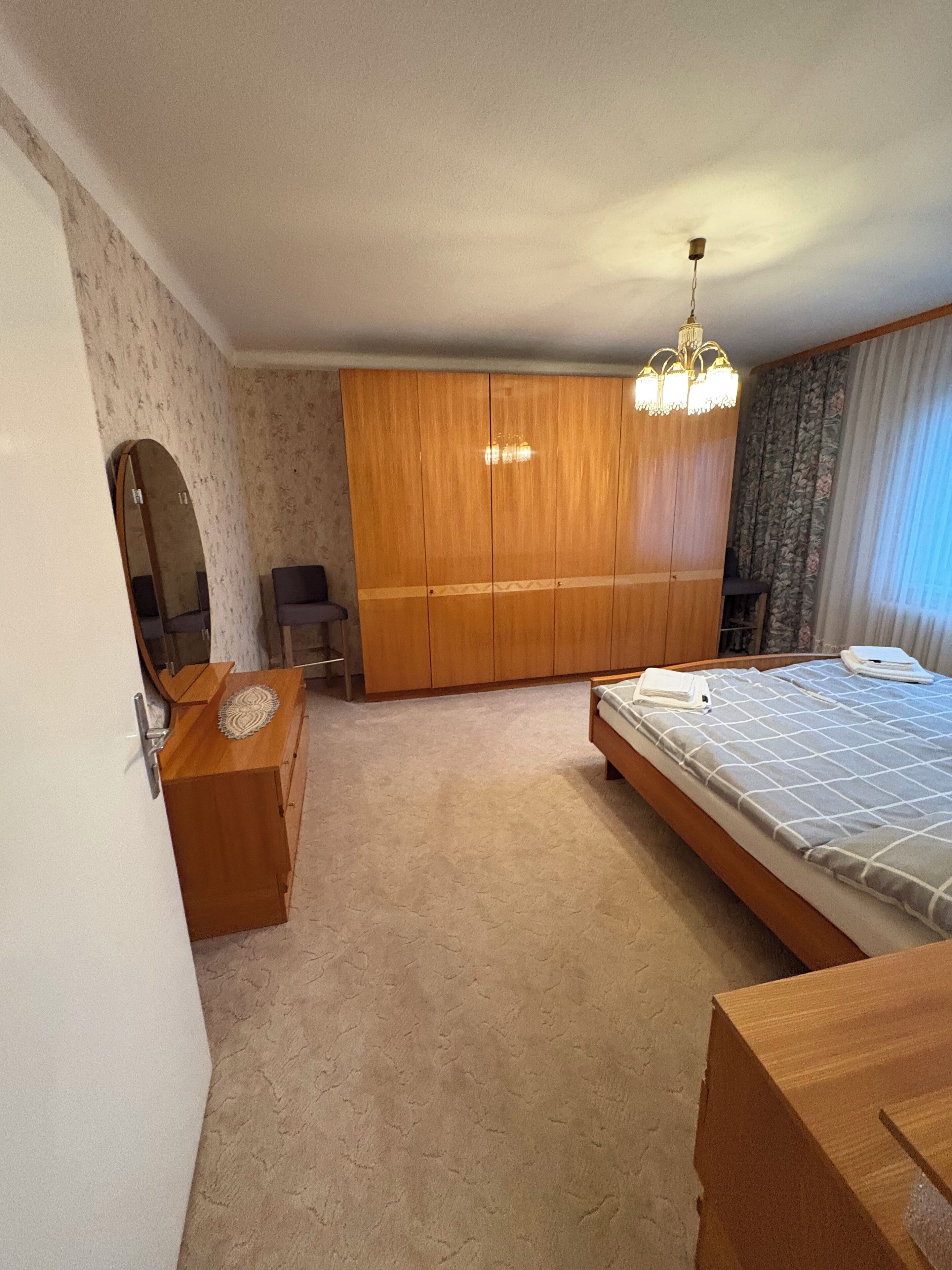 Un dormitorio con cama, armario de madera, escritorio y espejo.