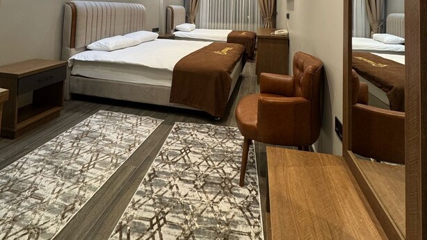 A modern hotel room with a large bed, a desk, a chair, a mirror, and a patterned rug. - Aydoğanlar Otel (Emirdag)
