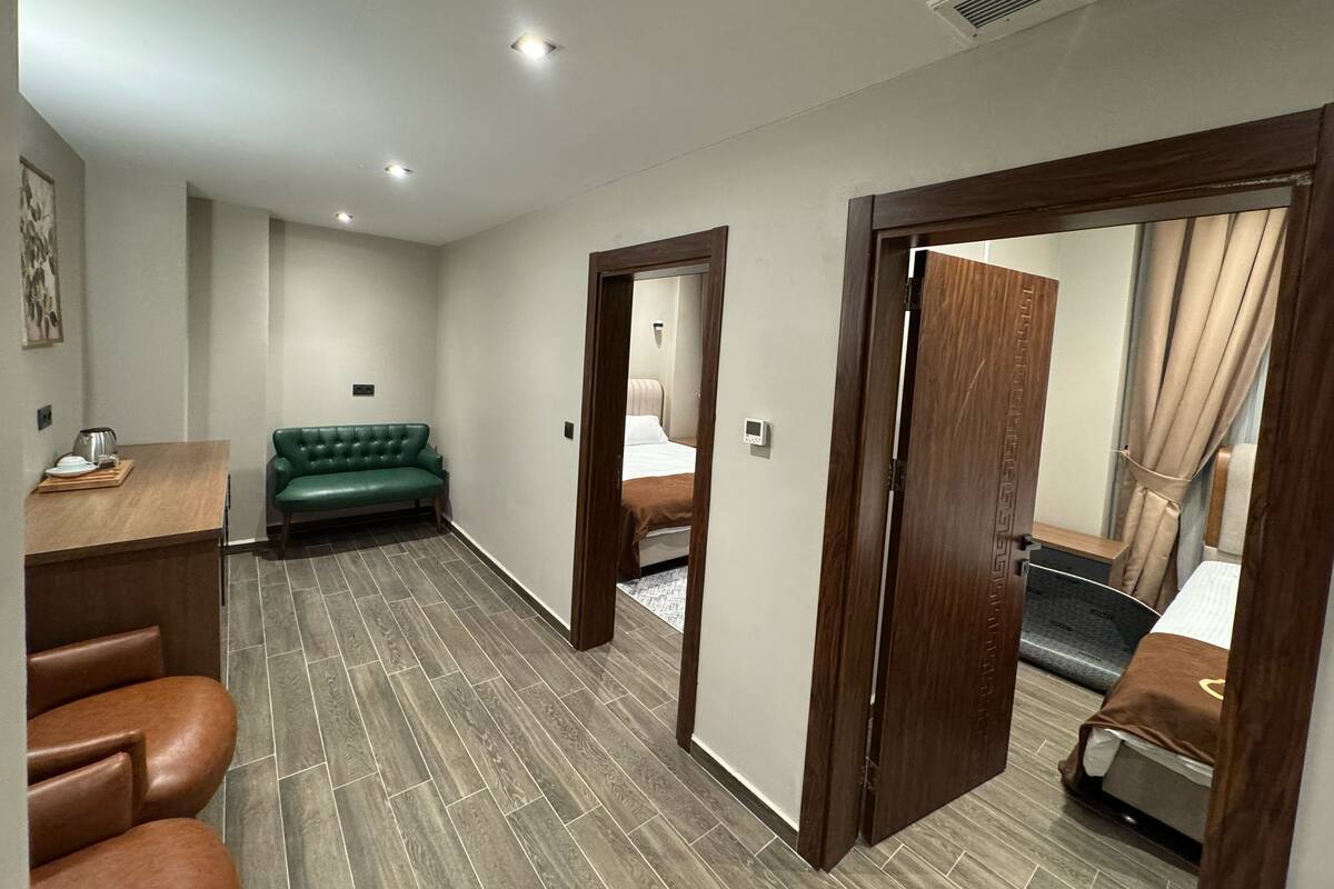 Habitación de hotel con escritorio de madera, sofá verde, sillón de cuero marrón y cama con manta marrón.