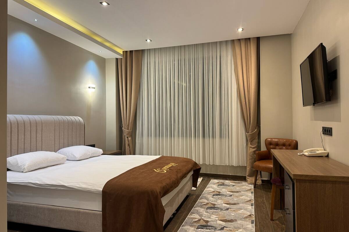 Una habitación de hotel moderna con cama, escritorio, silla, televisor y cortinas.