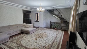 A spacious living room with a large patterned rug, a beige sectional sofa, a staircase, and a chandelier.