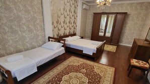 A hotel room with two single beds, a large ornate rug, a wooden wardrobe, and a chandelier.