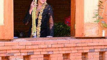 A person in traditional attire standing at a wooden doorway with a brick structure in the foreground.