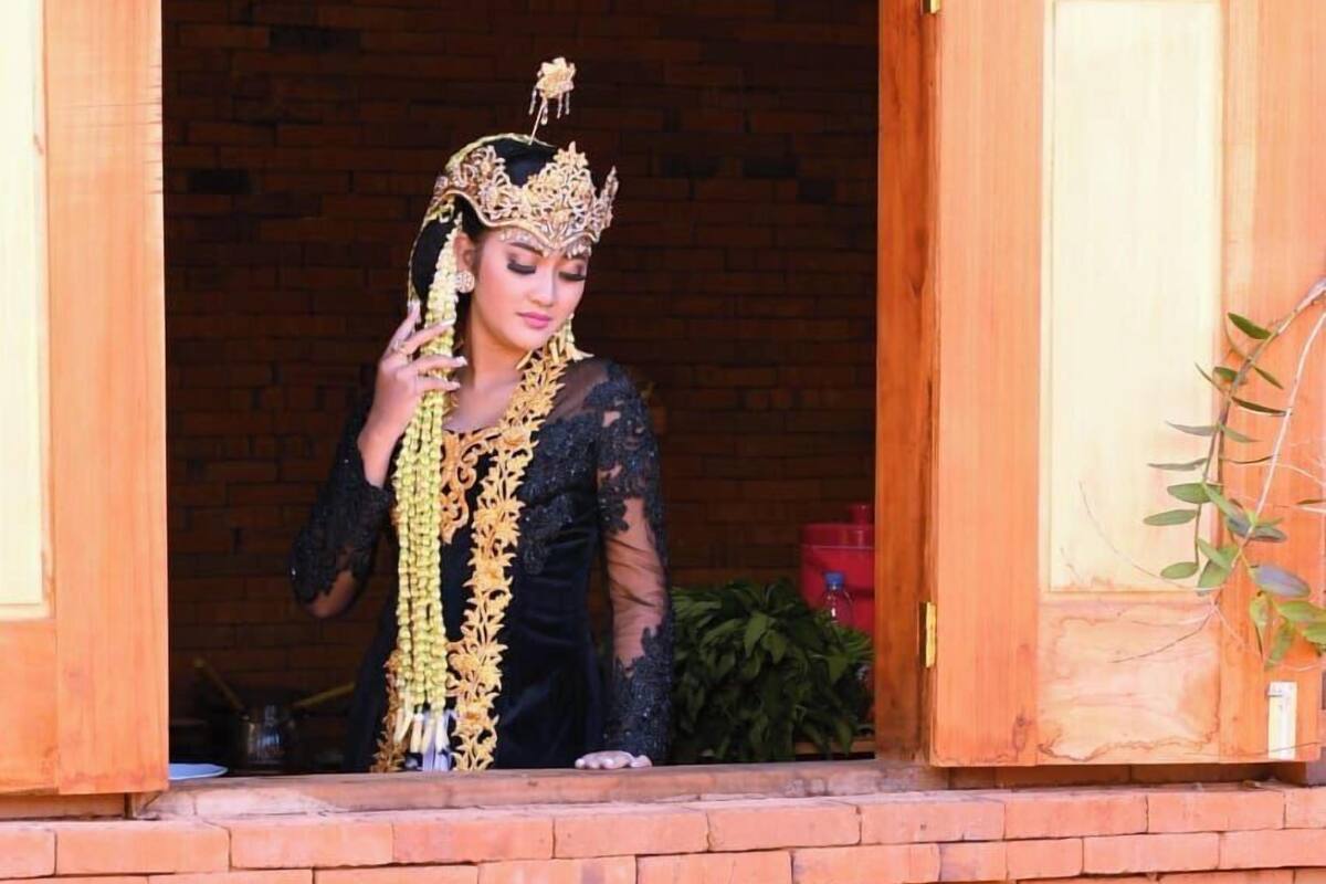 Uma pessoa vestindo traje tradicional em frente a uma porta de madeira com uma estrutura de tijolos.