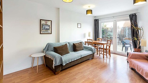 A living room with a sofa, a dining table, chairs, a small side table, and a large window with curtains.