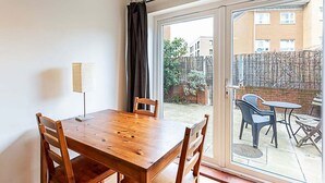 A room with a wooden dining table and chairs, a lamp, and a sliding glass door leading to an outdoor patio with a table and chairs.