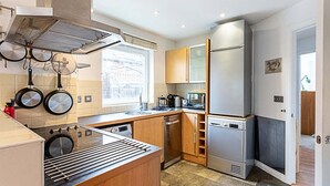 A modern kitchen with a gas stove, hanging pots, a dishwasher, and a refrigerator.