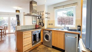 A modern kitchen with wooden cabinets, a built-in oven, a washing machine, and a dishwasher.
