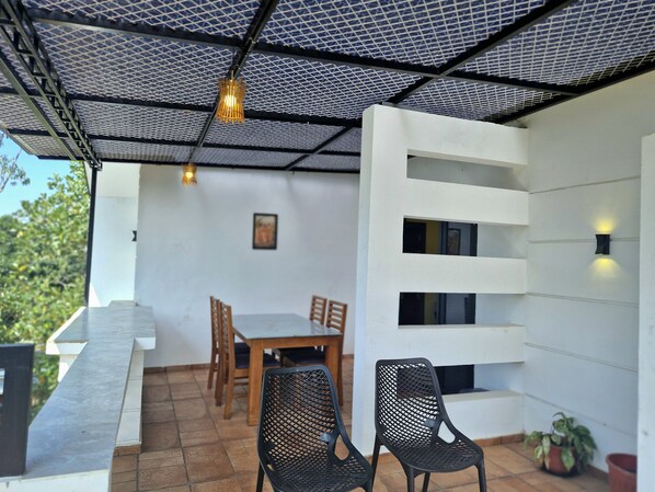An outdoor patio with a table and chairs, a white wall with built-in shelves, and a metal ceiling structure.