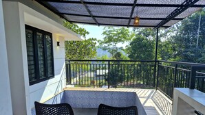 A balcony with two chairs, a table, and a view of greenery. - Scenic Mansion  Munnar (Anachal)