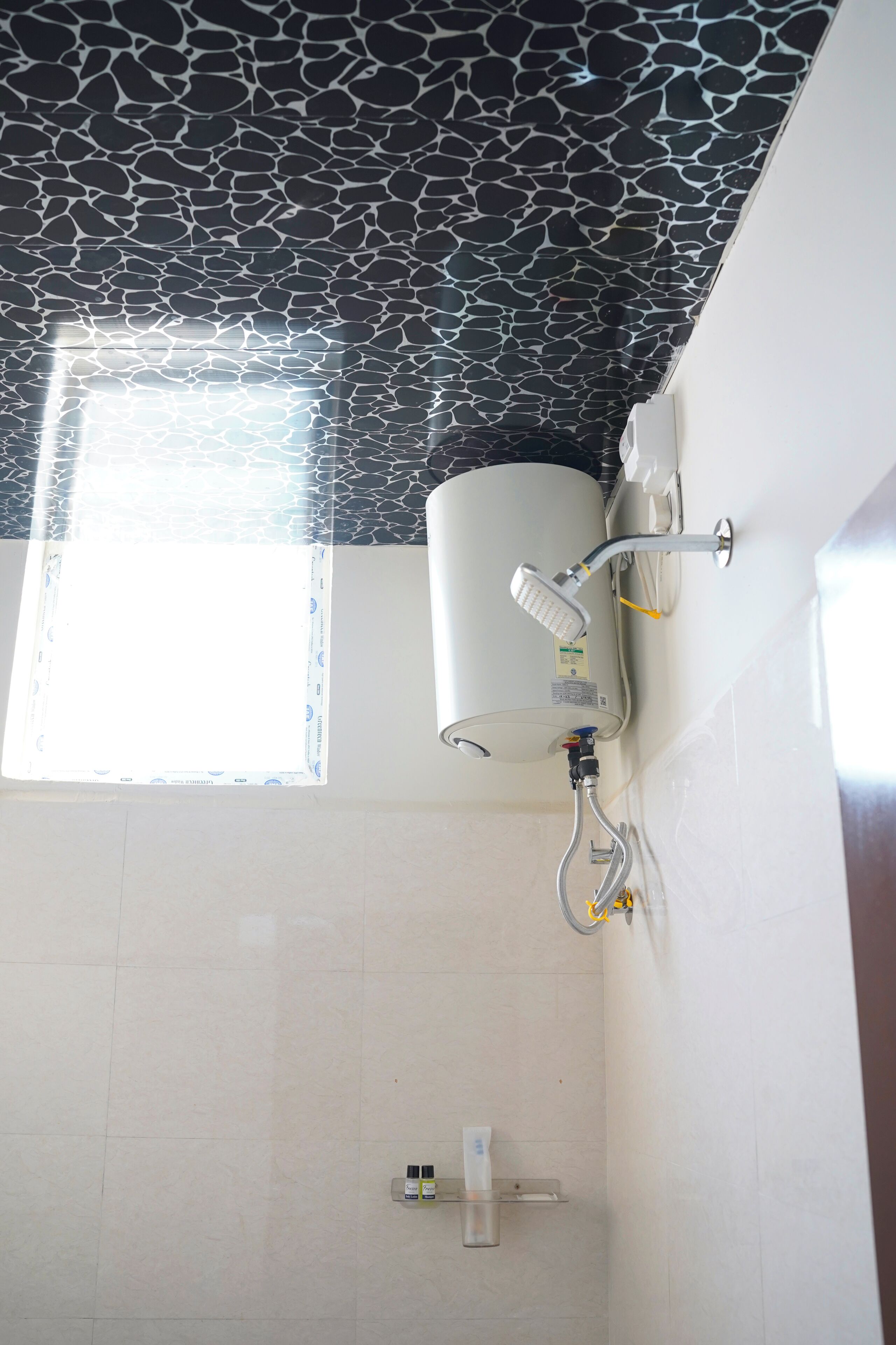 Un baño con calentador de agua montado en la pared, ventana con vistas y un estante pequeño con artículos de aseo.