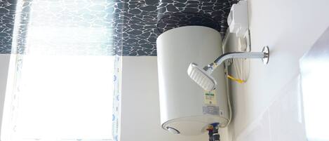 Un baño con calentador de agua montado en la pared, ventana con vistas y un estante pequeño con artículos de aseo.