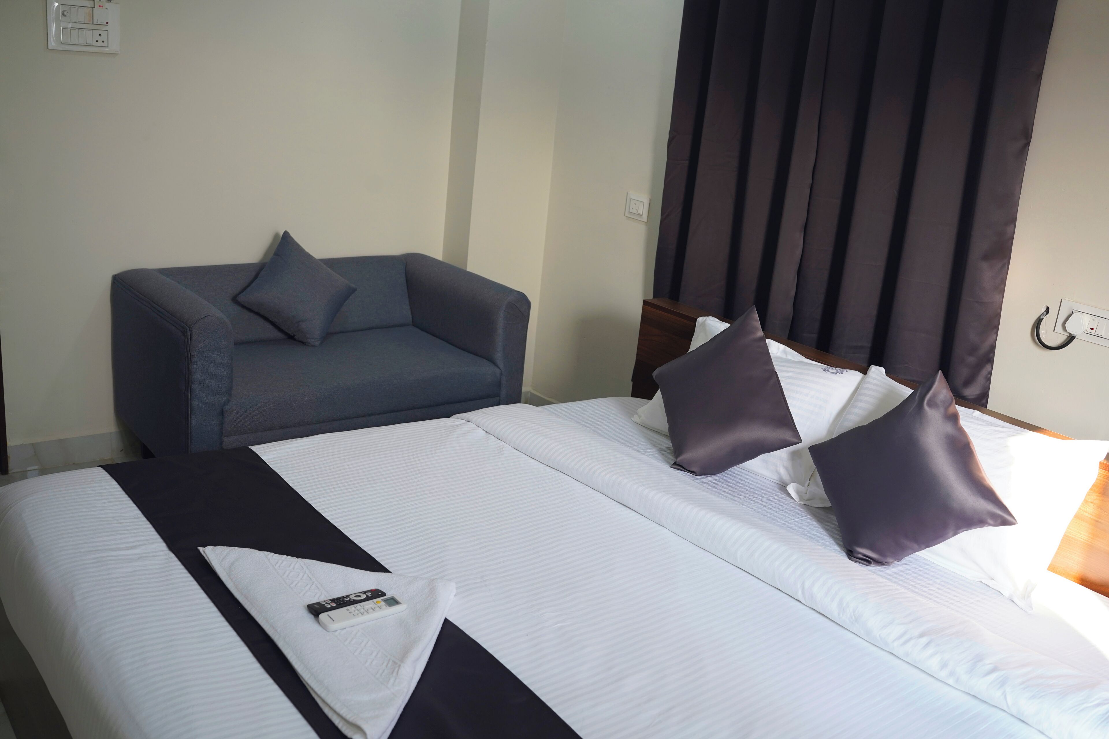 Une chambre d’hôtel avec un lit, un canapé gris et une fenêtre avec des rideaux foncés.